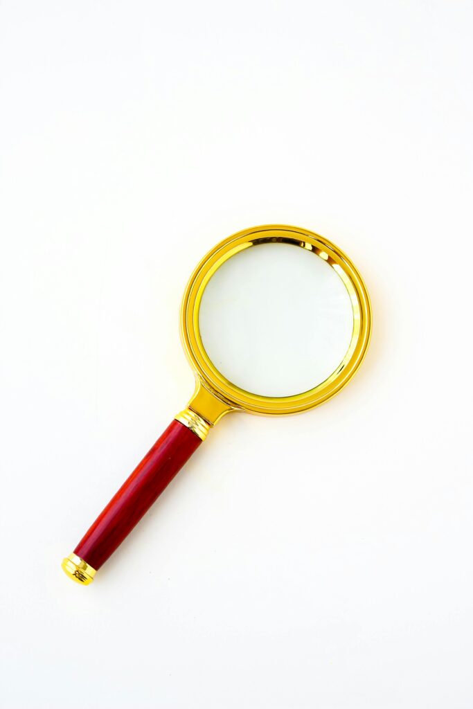 A luxury magnifying glass with a gold frame and red handle on a white background.